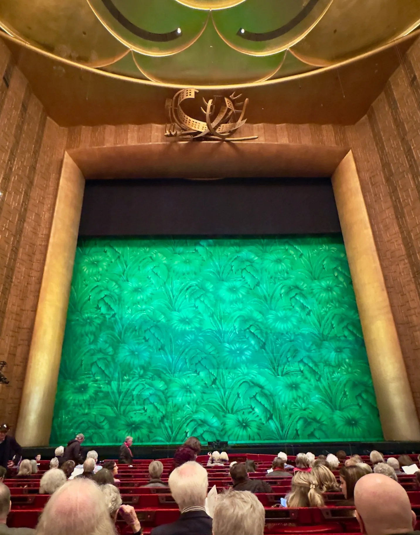 Metropolitan Opera house view of the green floral show curtain for Florencia en el Amazonas, gold proscenium and antlered chandelier above
